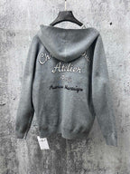 Gray zip-up hoodie with printed “Atelier Paris” text on back