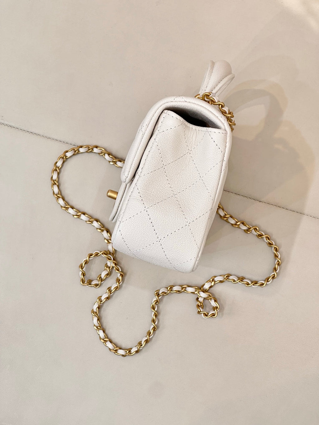 Chanel quilted mini flap bag side view, white leather with gold chain shoulder strap