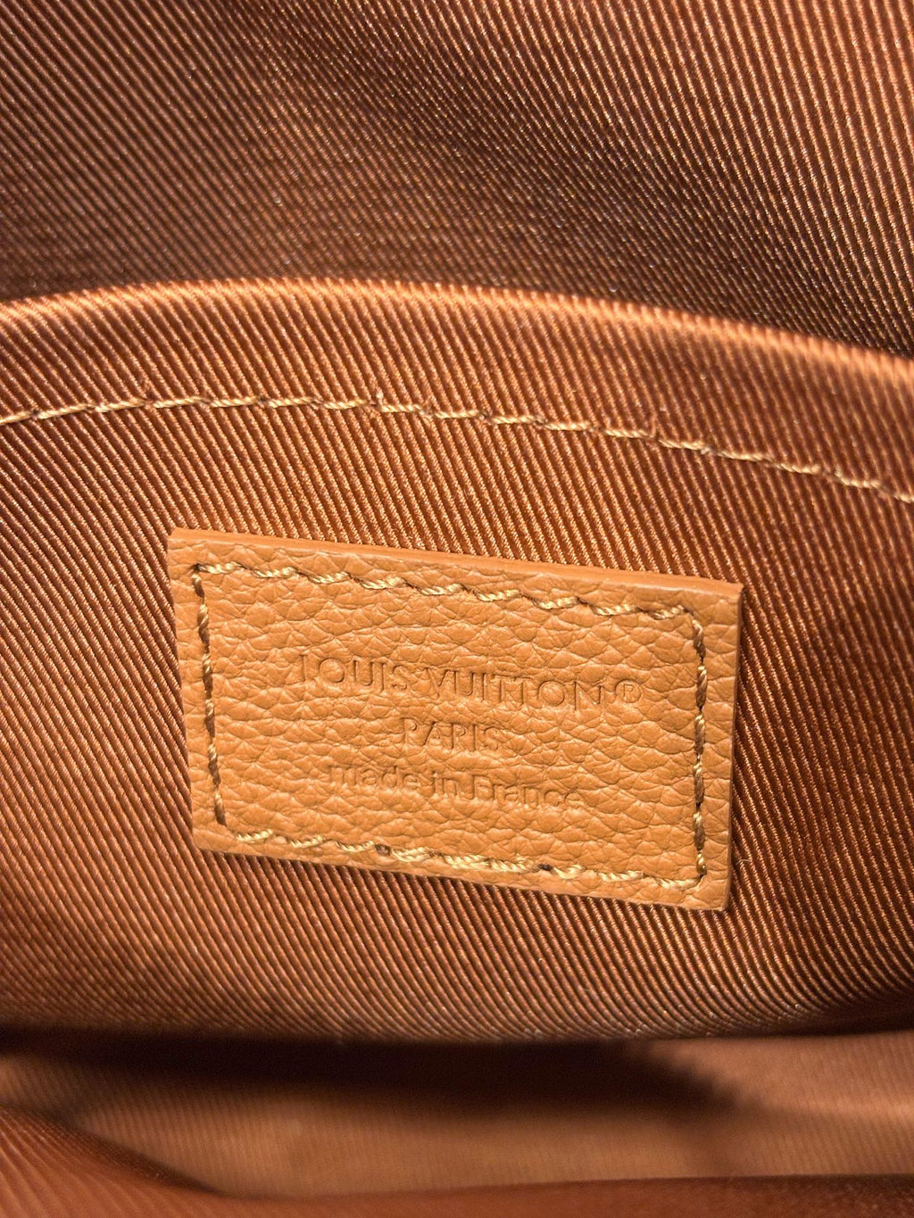 Close-up of Louis Vuitton tan leather bag logo patch with stitched edges