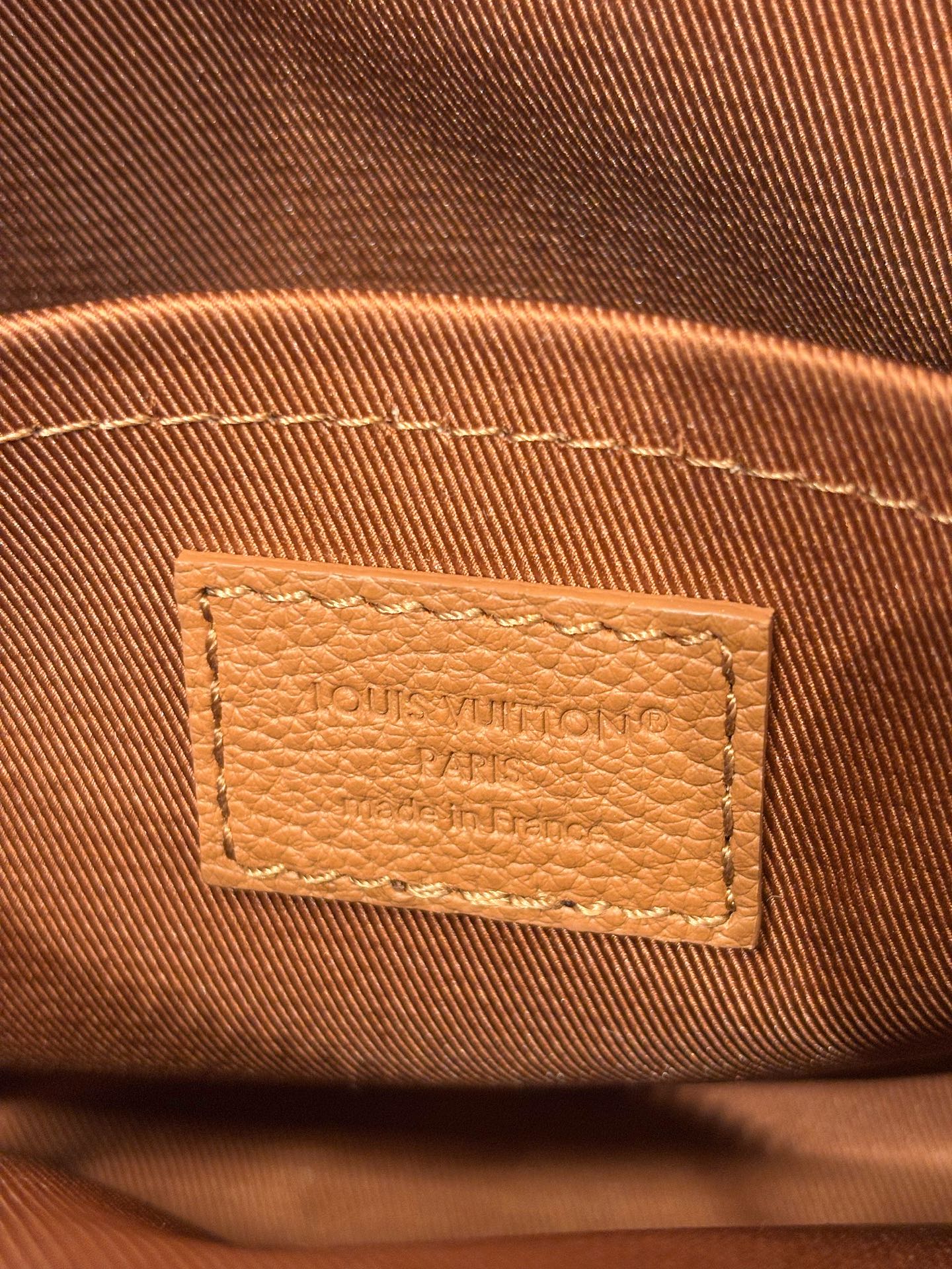Close-up of Louis Vuitton tan leather bag logo patch with stitched edges