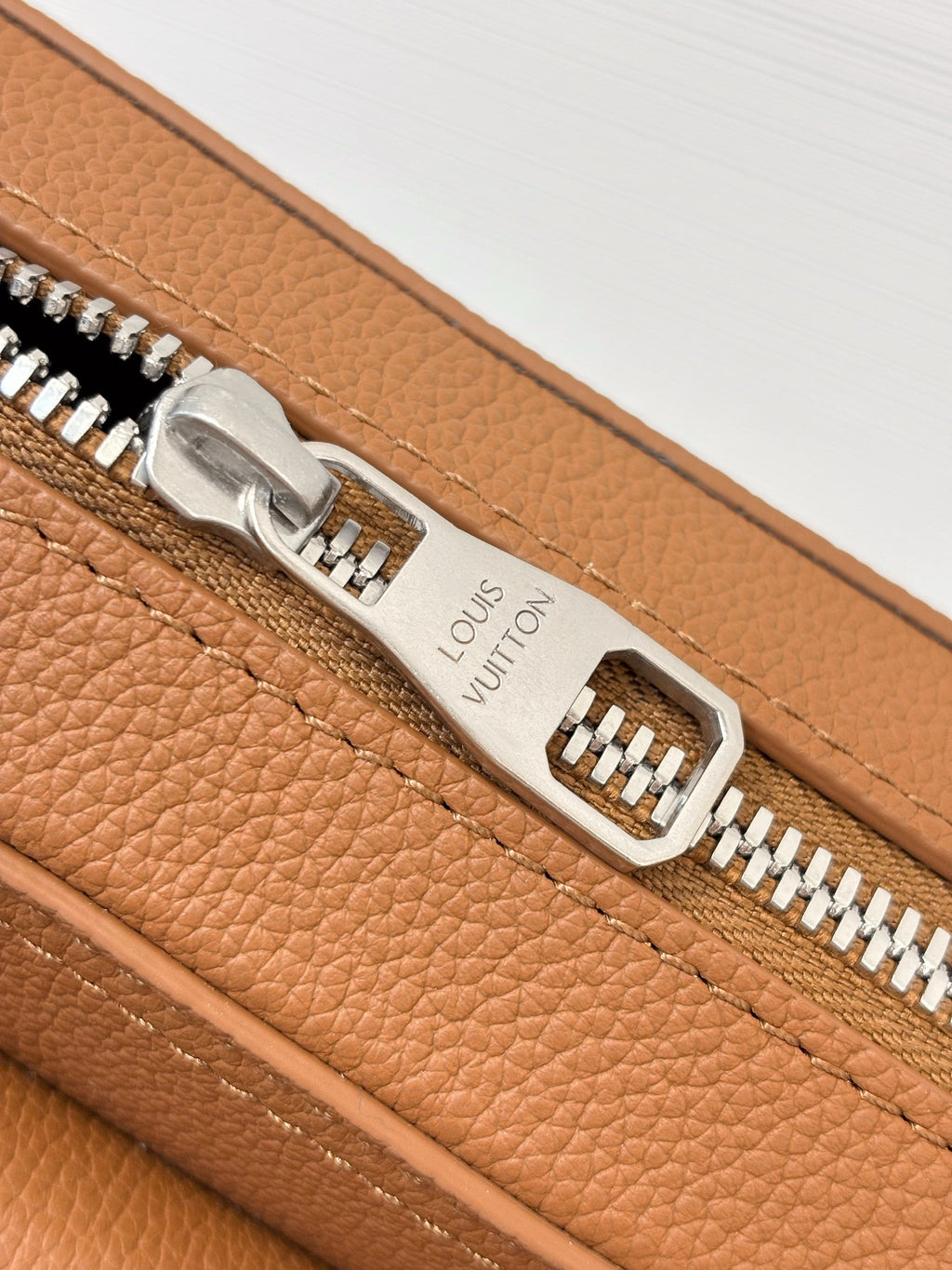 Close-up of Louis Vuitton bag zipper and engraved pull tab on tan leather