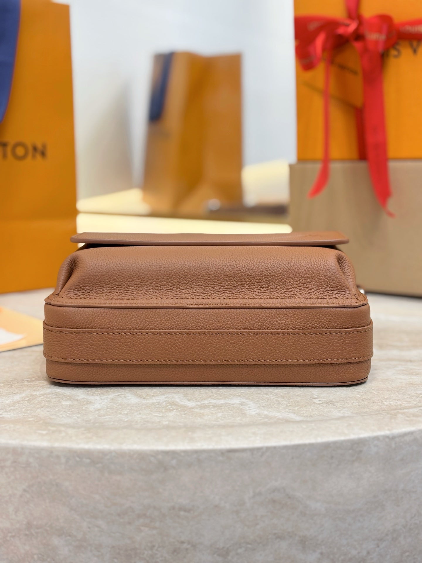 Tan leather Louis Vuitton crossbody bag shown from side with flap and strap loops