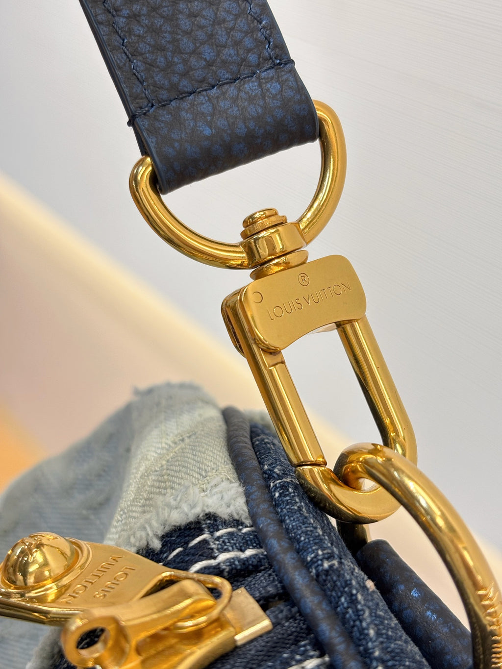 Louis Vuitton denim handbag close-up of gold-tone clasp and keyring hardware on strap