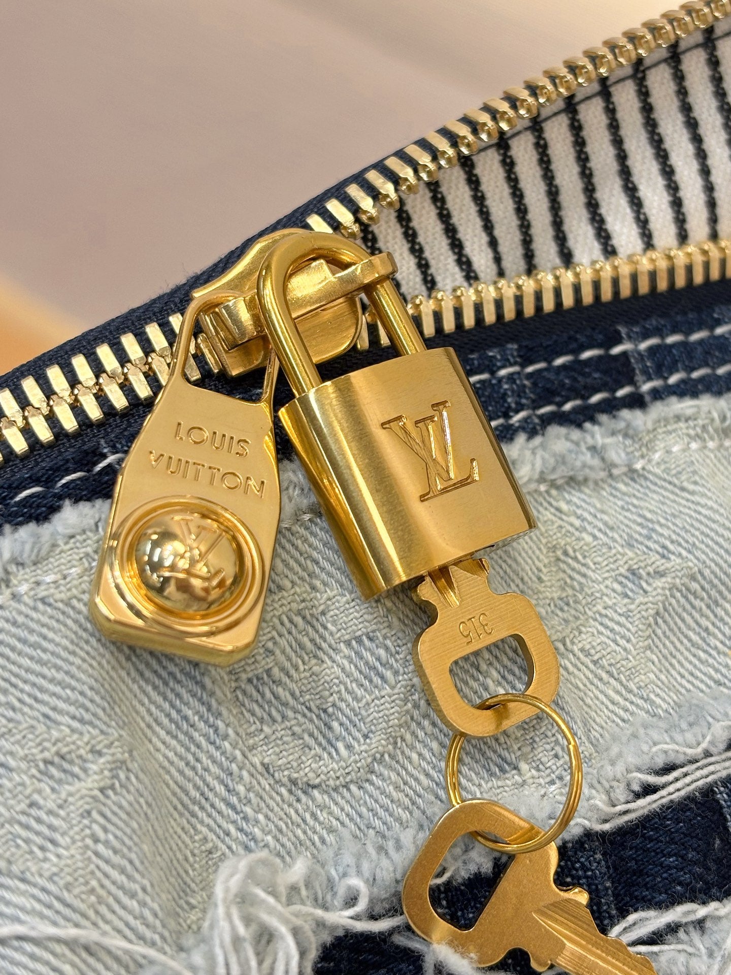 Louis Vuitton denim handbag close-up of gold-tone zipper pull and hardware on fabric
