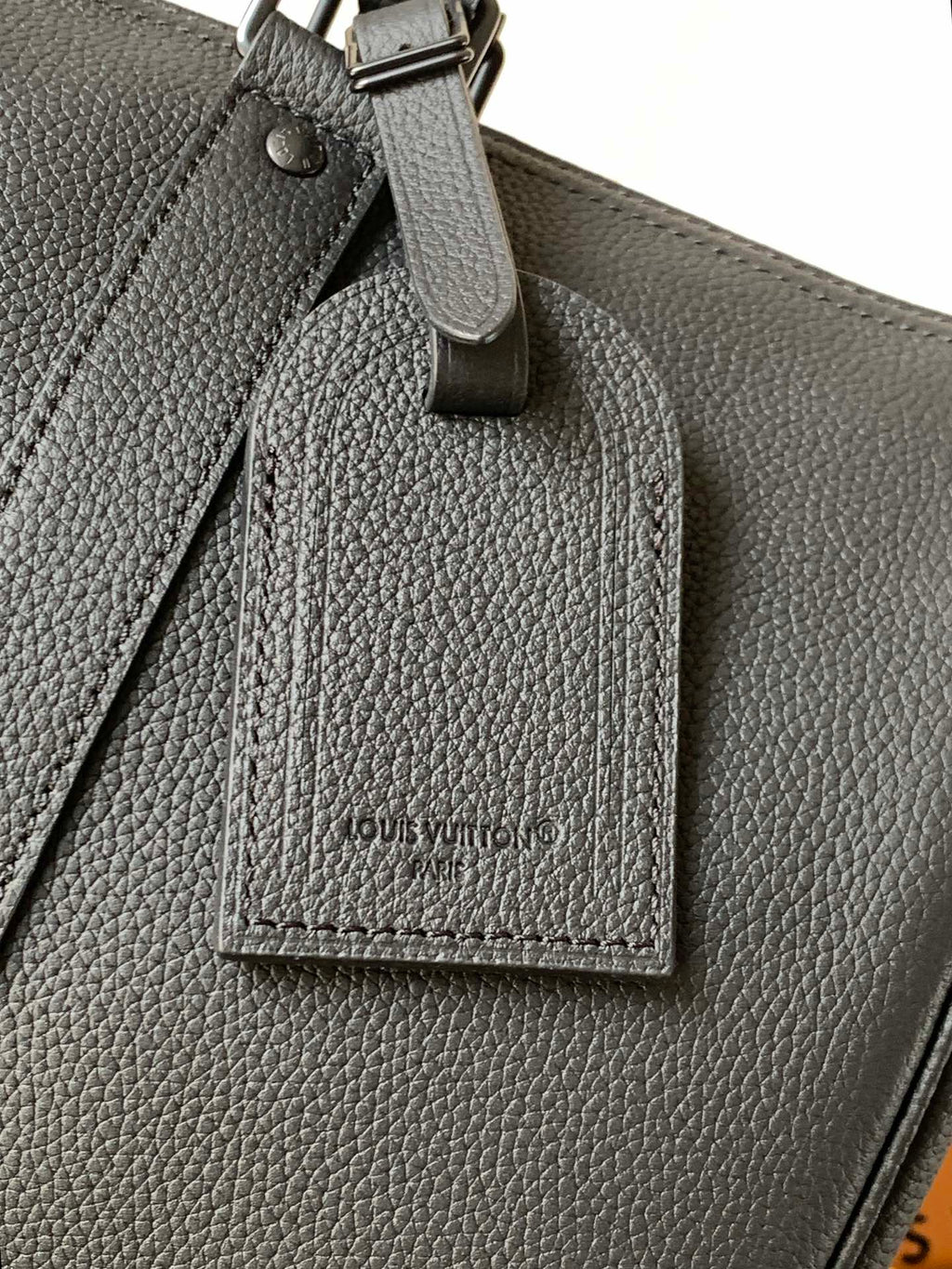 Dark leather tag hanging from handbag with Louis Vuitton name