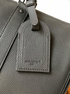 Dark leather tag hanging from handbag with Louis Vuitton name
