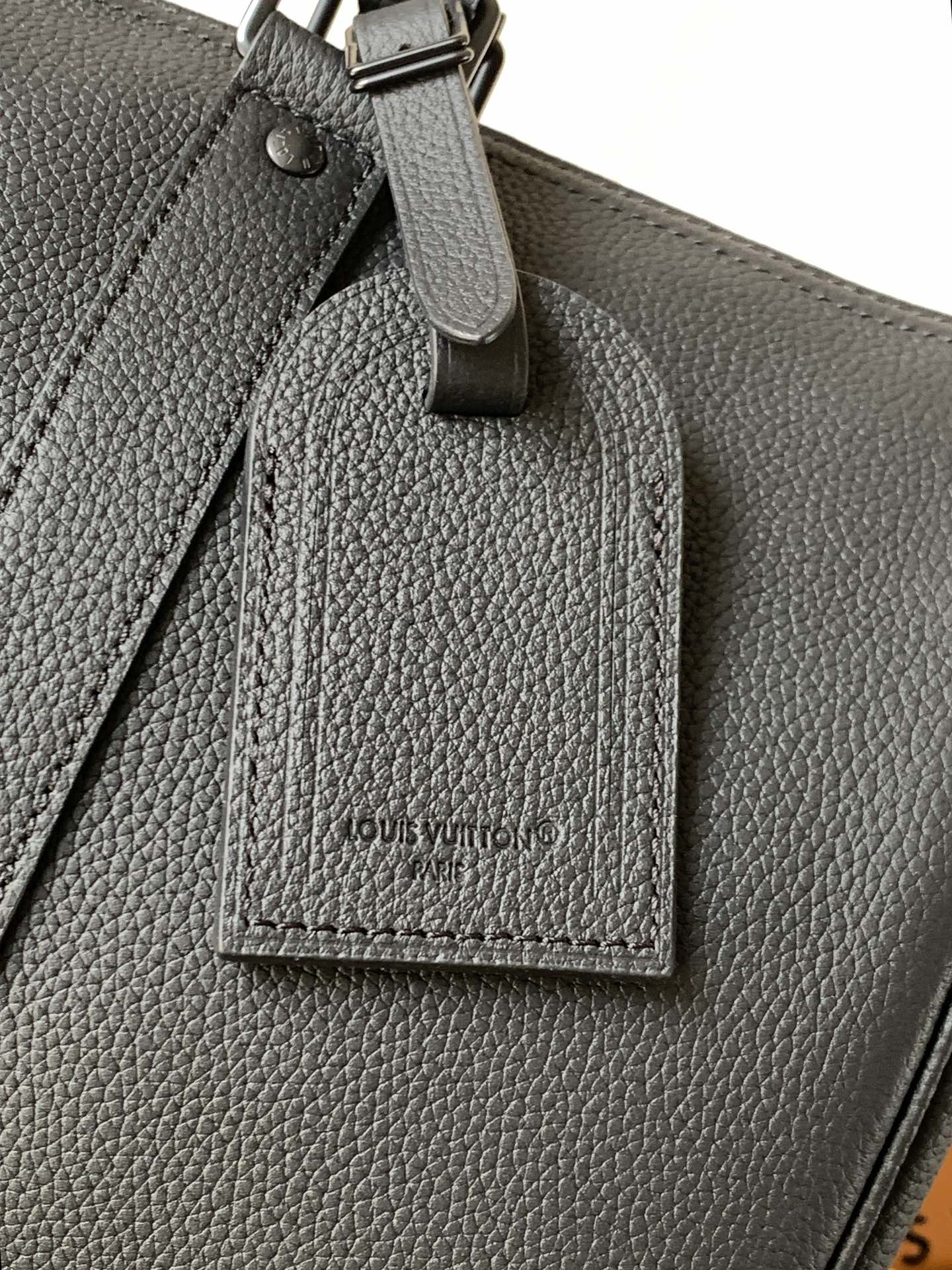 Dark leather tag hanging from handbag with Louis Vuitton name