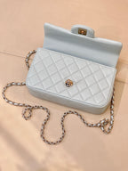 Light blue quilted handbag with flap, gold-tone emblem, chain shoulder strap and top handle