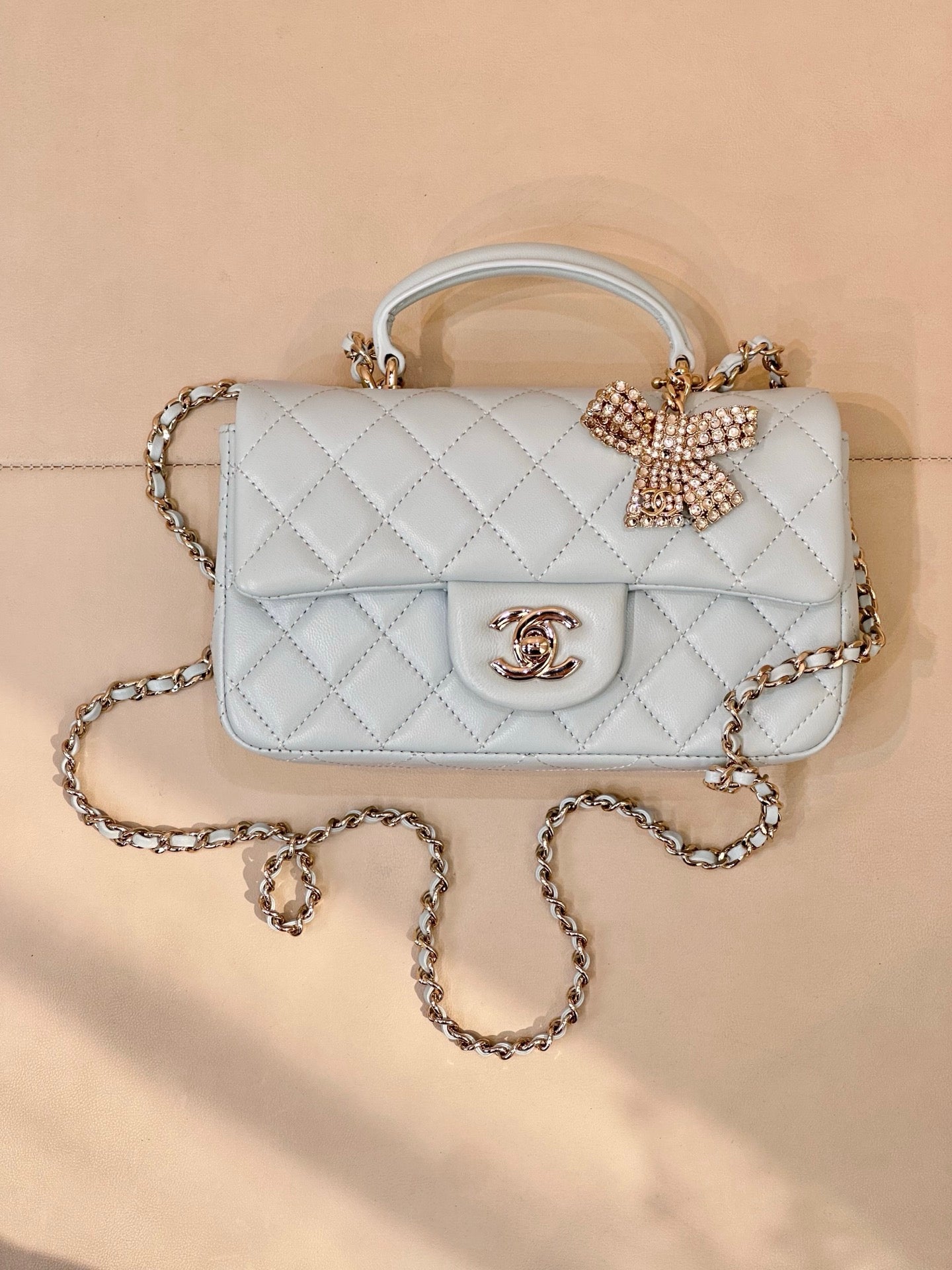 Light blue quilted handbag, front flap with gold-tone logo, bow embellishment, chain strap