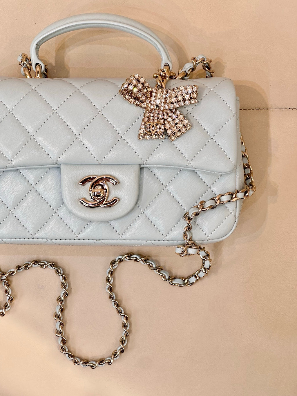 Light blue quilted handbag close-up, flap with gold-tone logo and beaded bow, chain strap