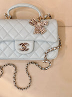 Light blue quilted handbag close-up, flap with gold-tone logo and beaded bow, chain strap