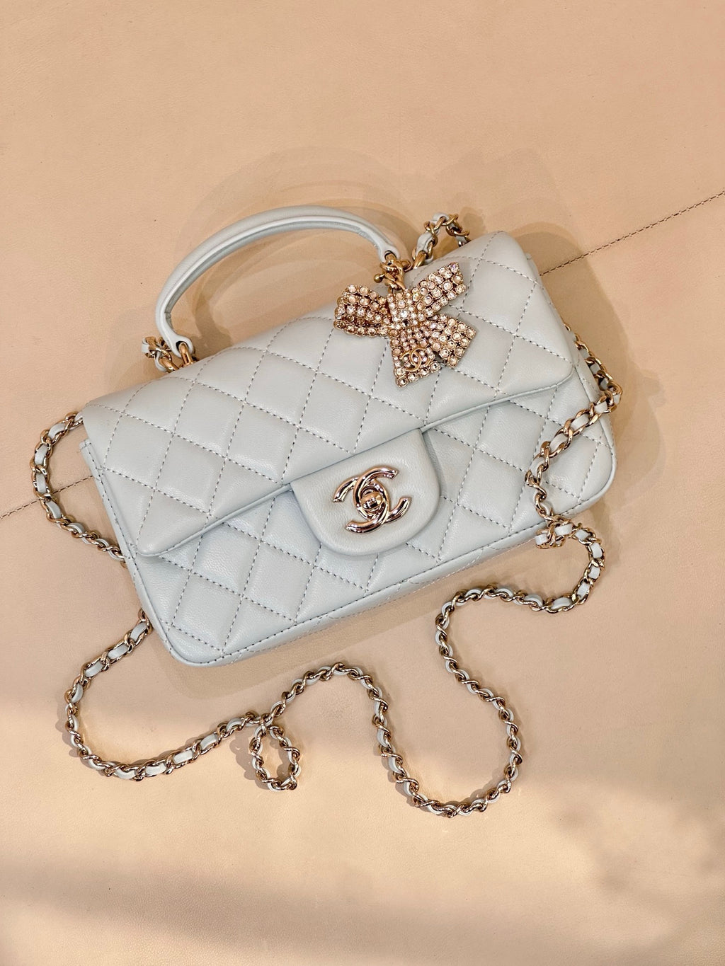 Light blue quilted handbag with flap, gold-tone logo, bow embellishment, short top handle