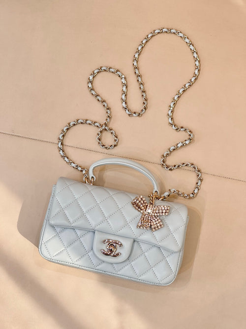Light blue quilted handbag with flap, gold-tone logo, bow charm, chain shoulder strap