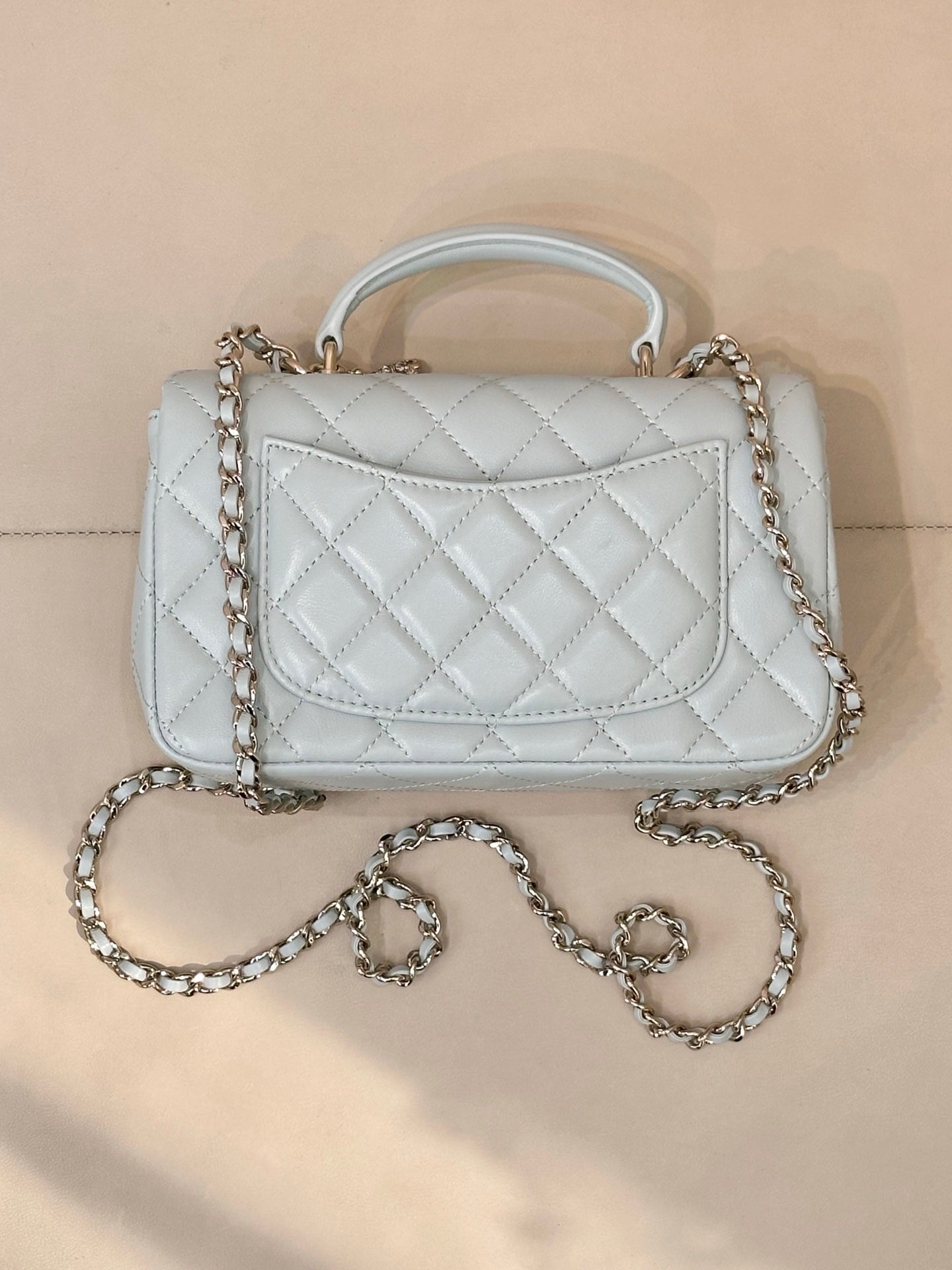 Light blue quilted handbag with front flap, gold-tone logo, chain shoulder strap