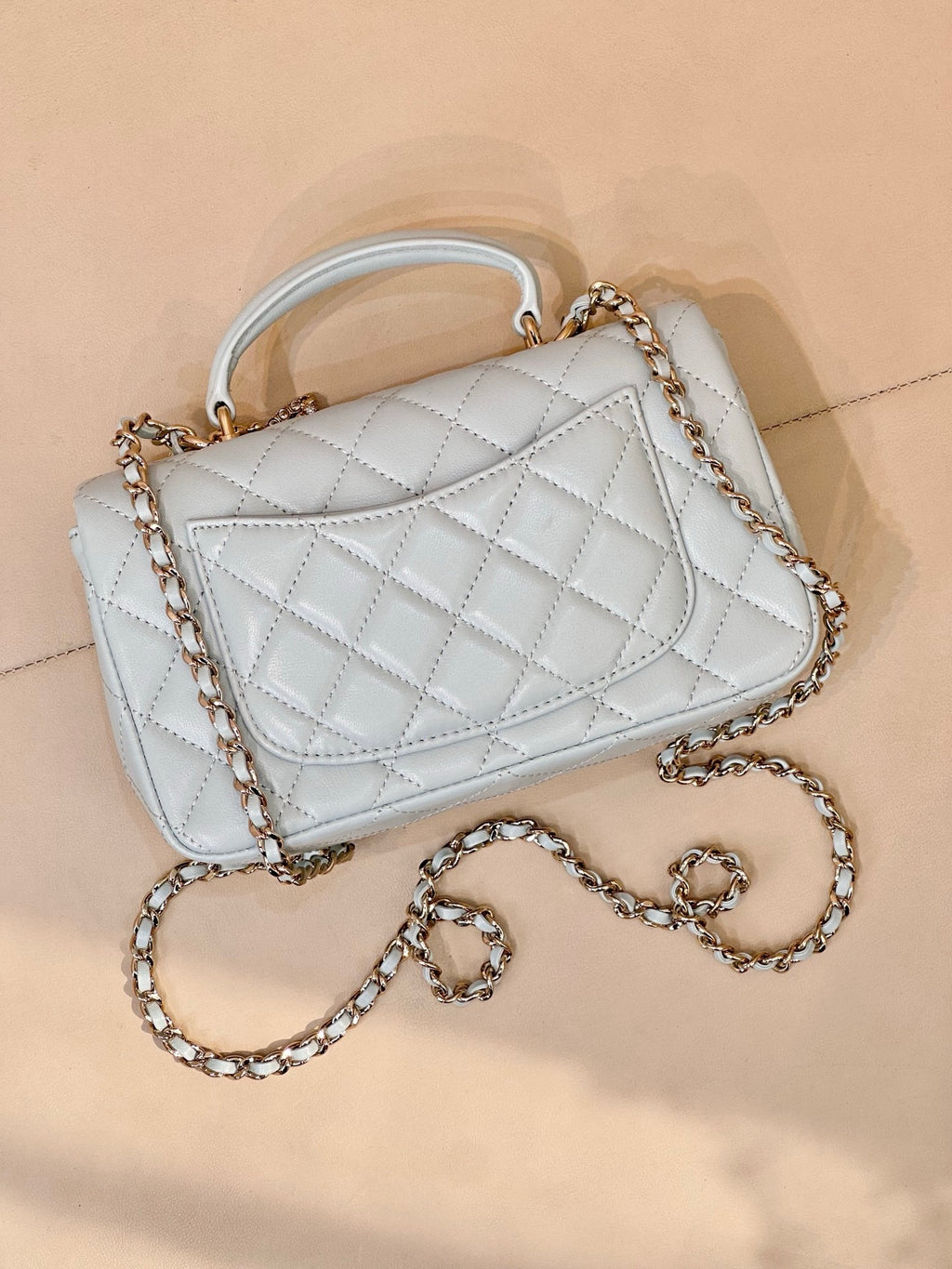 Light blue quilted handbag with front flap, gold-tone logo, chain strap, quilted pattern