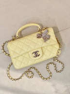 Light yellow quilted flap bag with gold chain shoulder strap and Chanel logo, bow embellishment.