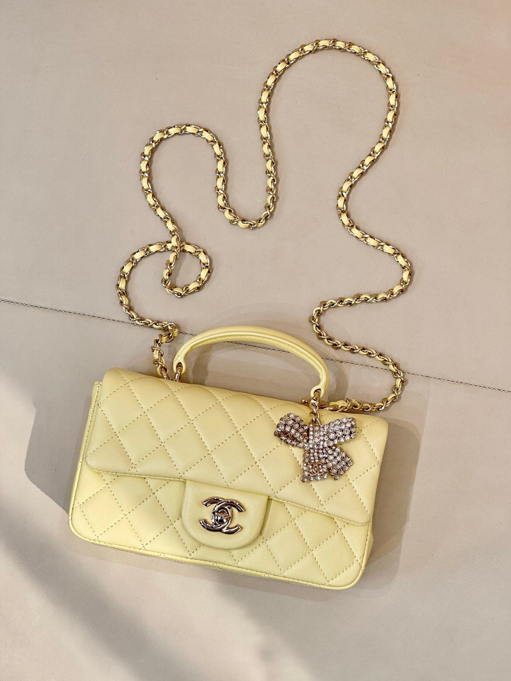 Light yellow quilted flap shoulder bag with gold chain strap and Chanel logo, bow charm.