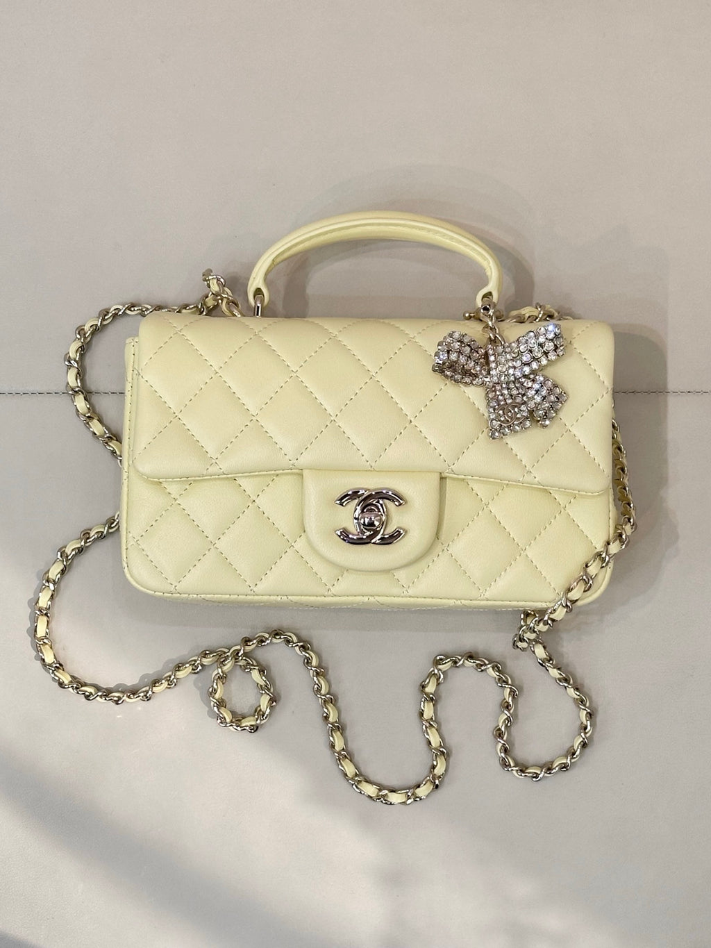 Light yellow quilted shoulder bag with top handle and gold chain strap, Chanel logo front.