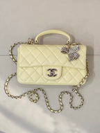 Light yellow quilted shoulder bag with top handle and gold chain strap, Chanel logo front.