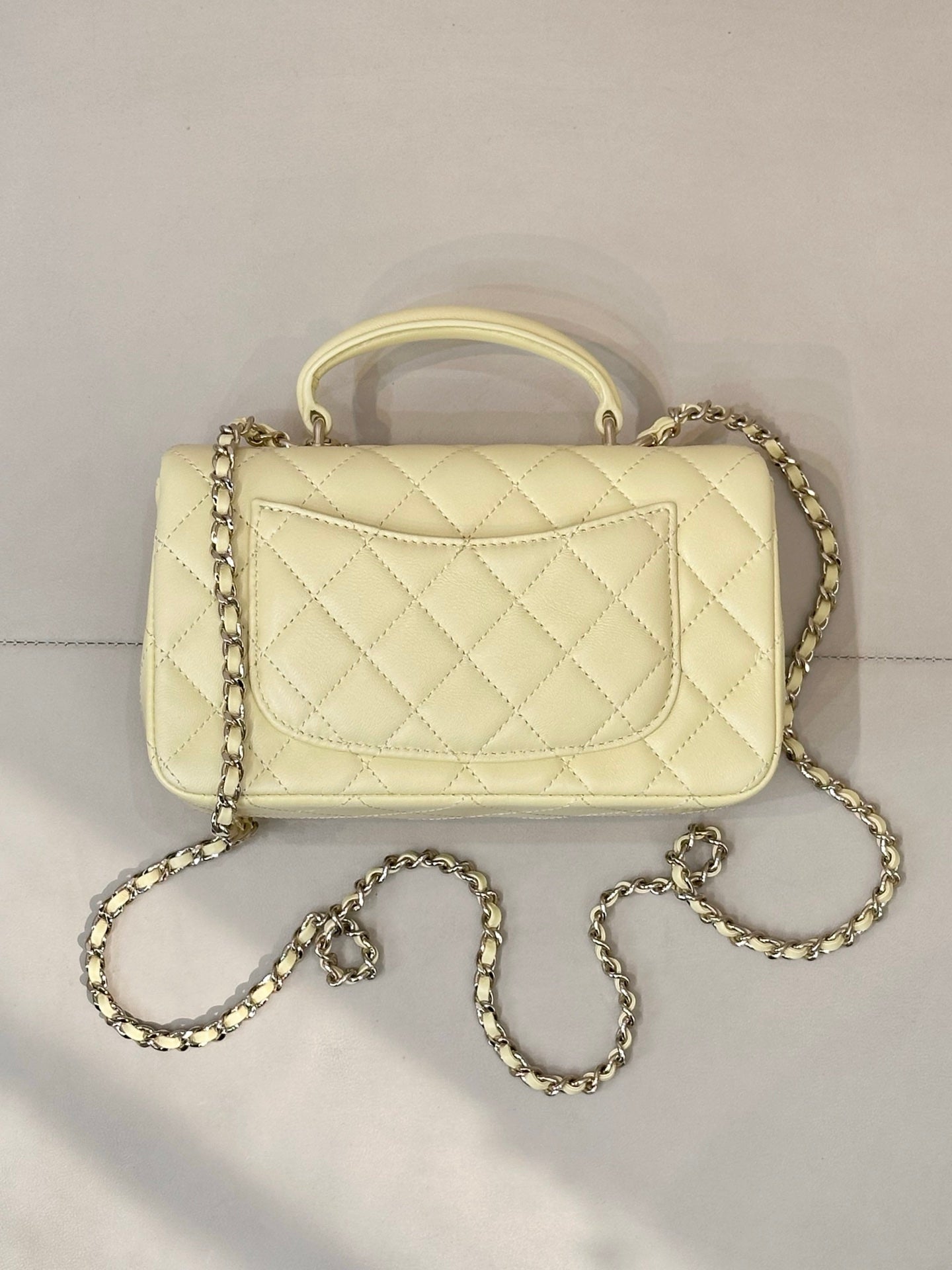 Light yellow quilted mini shoulder bag with gold chain strap and front flap panel design.