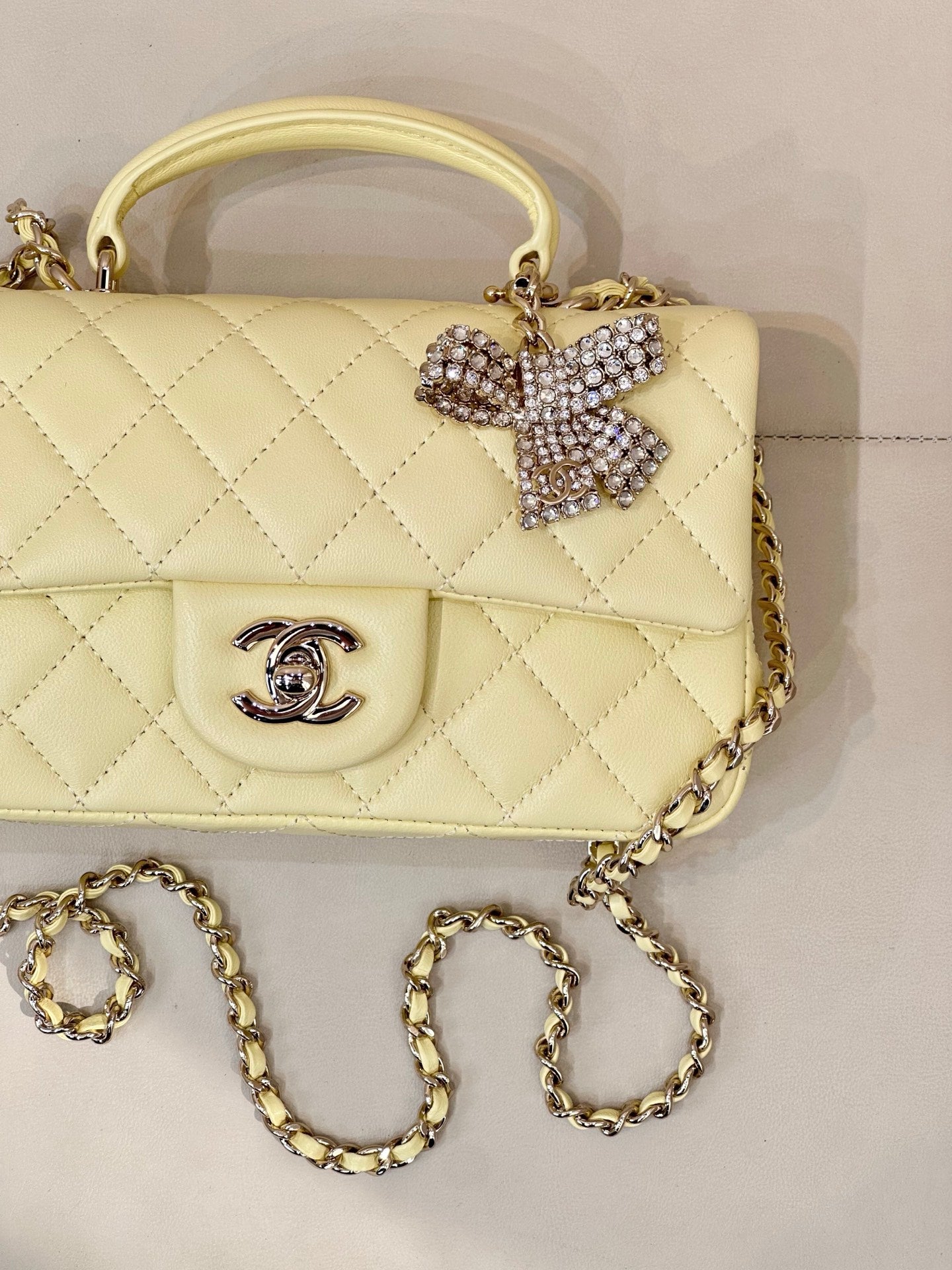 Close-up light yellow quilted flap bag with Chanel logo and gold chain strap, bow charm detail.