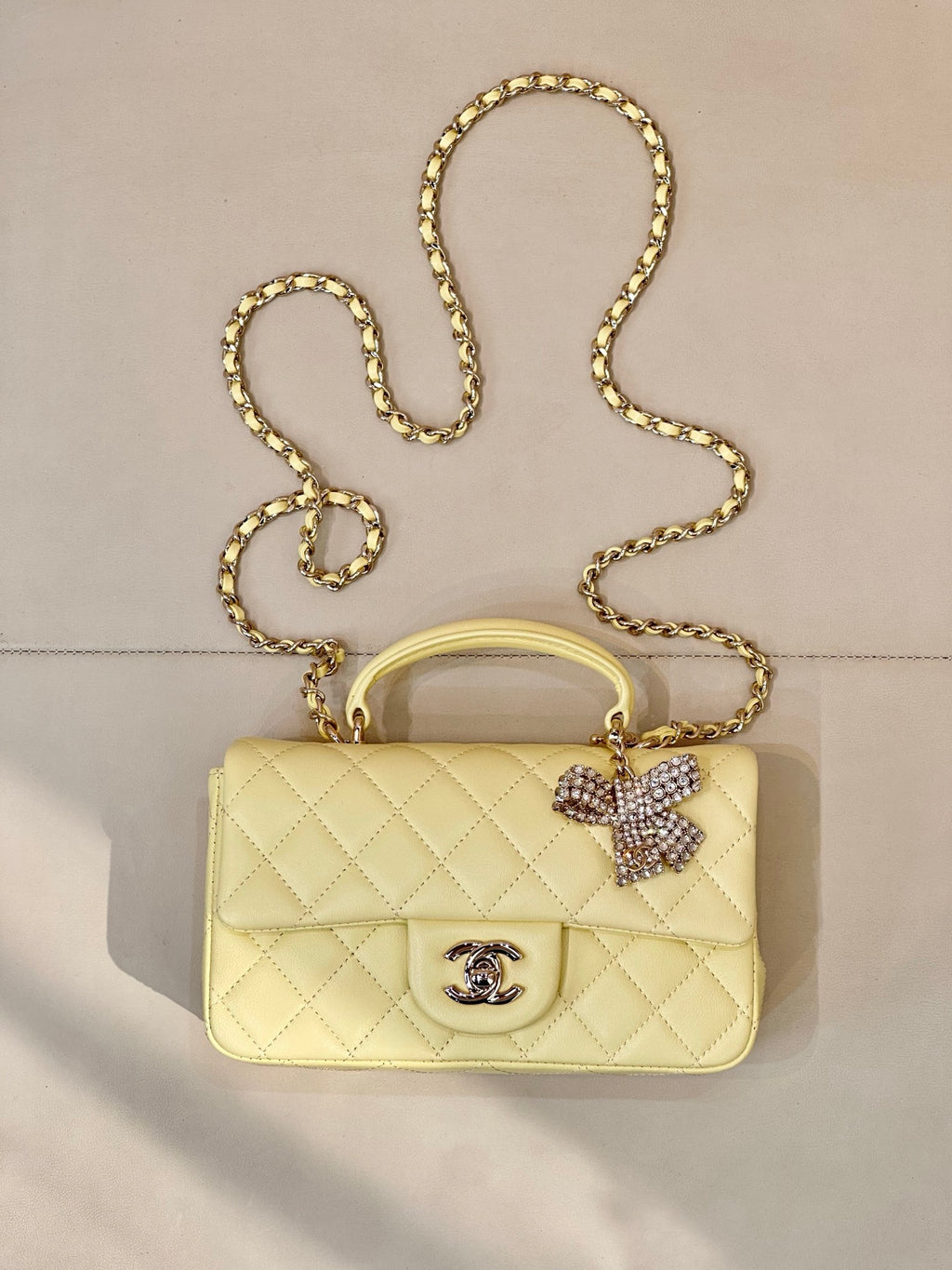 Light yellow quilted shoulder bag with gold chain strap and Chanel logo front.