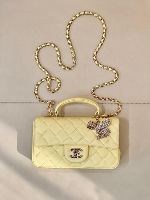 Light yellow quilted shoulder bag with gold chain strap and Chanel logo front.