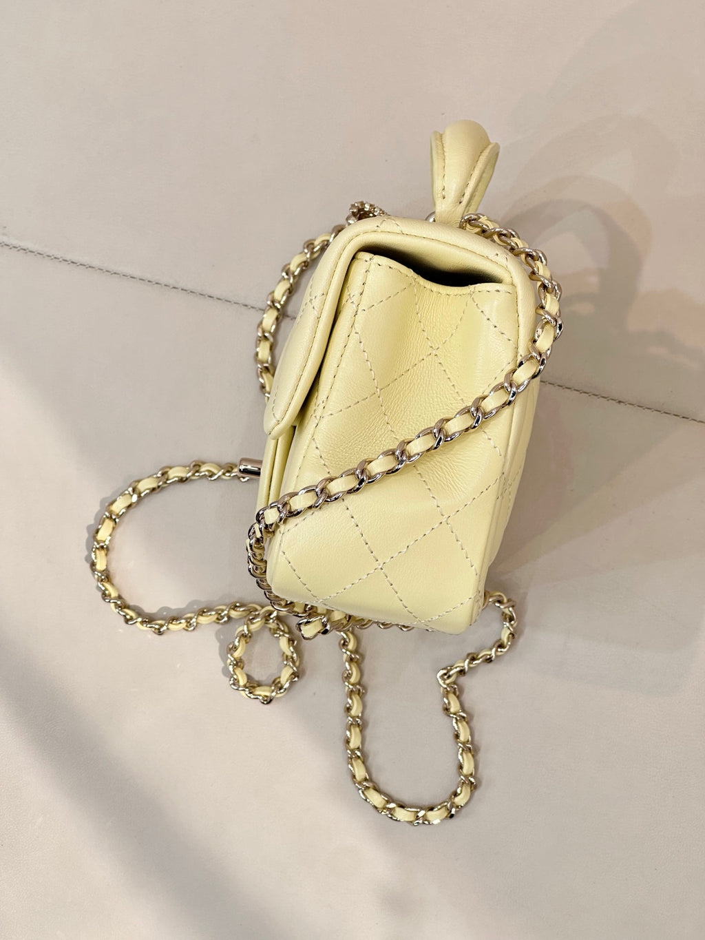 Light yellow quilted mini bag with gold chain strap, side view with top handle.