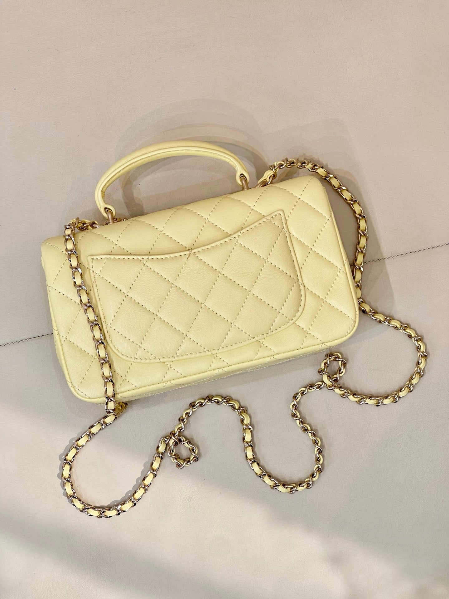 Light yellow quilted flap mini shoulder bag with gold chain strap and Chanel logo front.