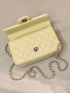 Light yellow quilted crossbody bag with gold chain strap and small round stud at front.