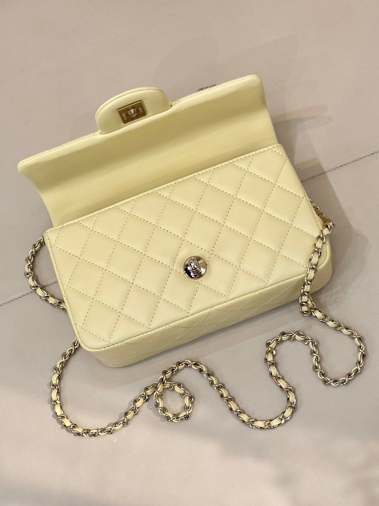 Light yellow quilted crossbody bag with gold chain strap and small round stud at front.