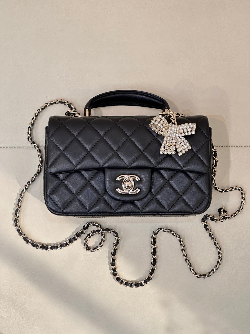 Dark quilted leather crossbody bag with chain strap, logo medallion, bow detail