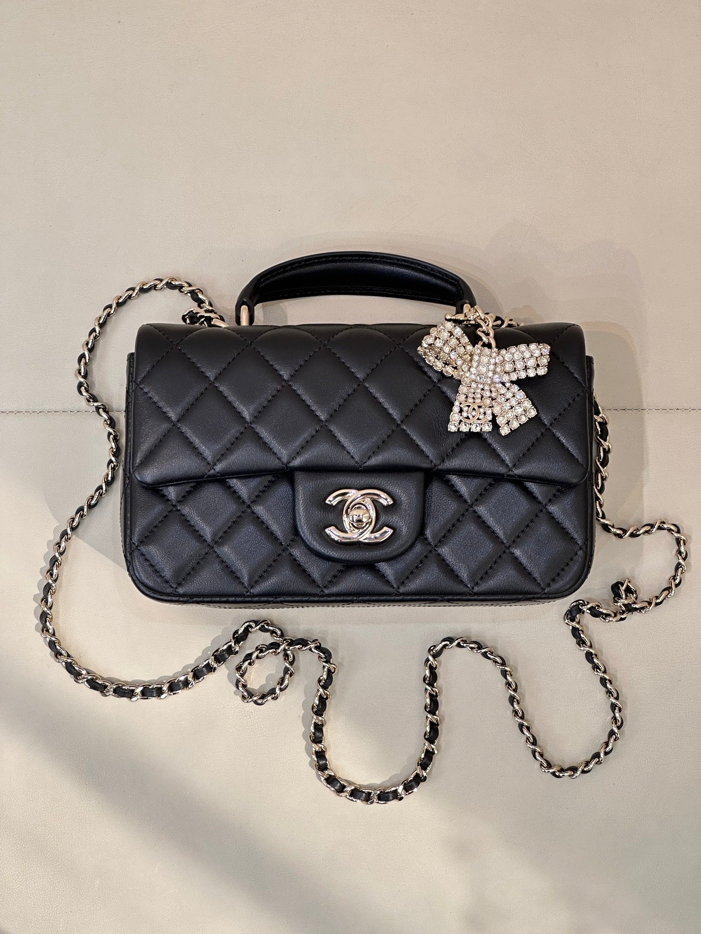 Dark quilted leather crossbody bag with chain strap, logo medallion, bow detail