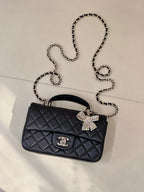 Dark quilted leather flap bag with chain strap, bow embellishment, and logo charm