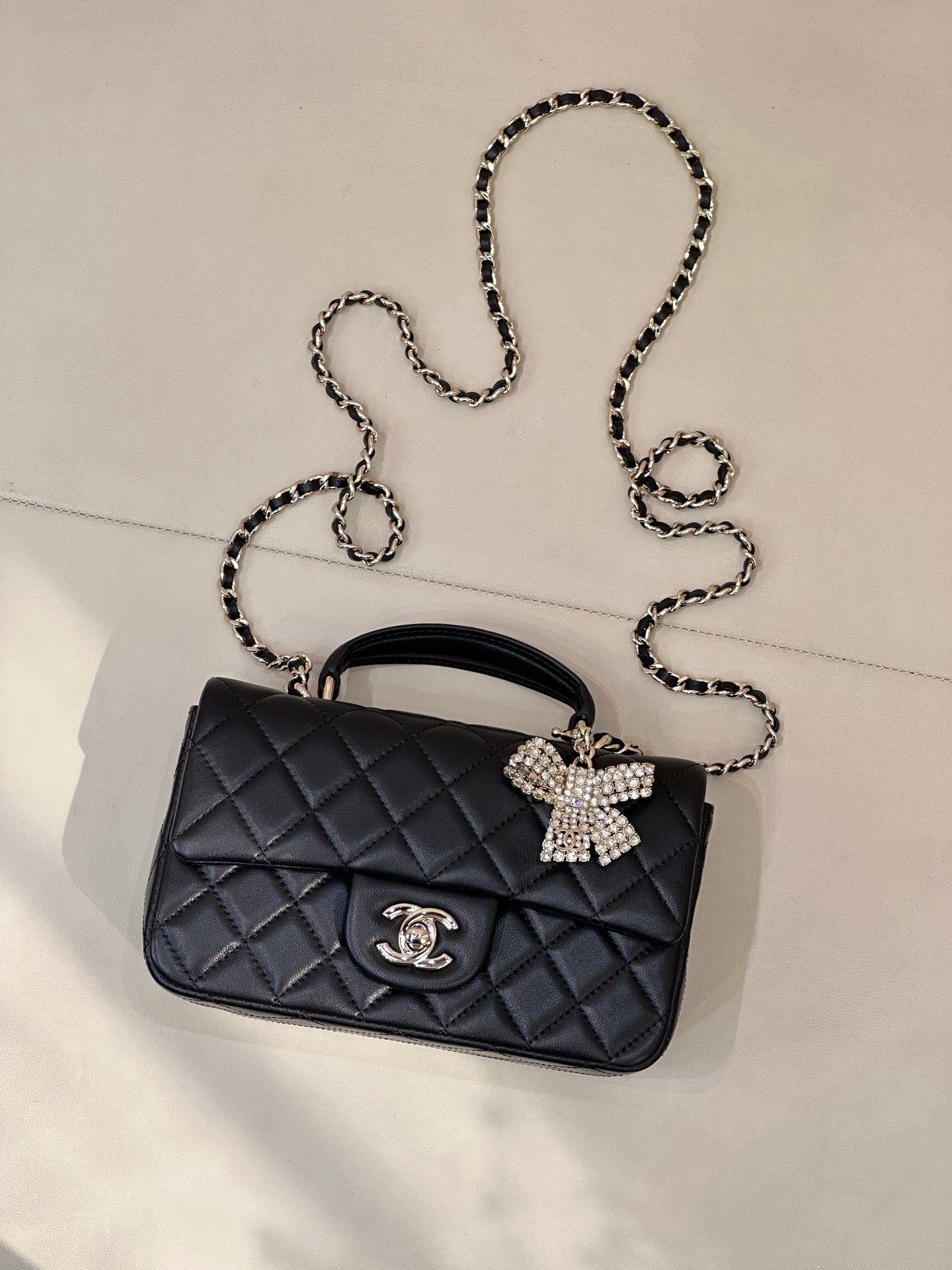 Dark quilted leather flap bag with chain strap, bow embellishment, and logo charm