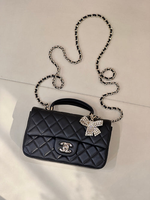 Dark quilted leather flap bag with chain strap, bow embellishment, and logo charm