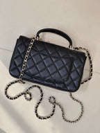 Dark quilted leather flap handbag angled view with top handle and chain shoulder straps