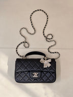 Dark quilted leather shoulder bag with chain strap and decorative bow clasp