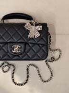 Dark quilted leather flap bag close-up with logo emblem, chain strap, bow clasp