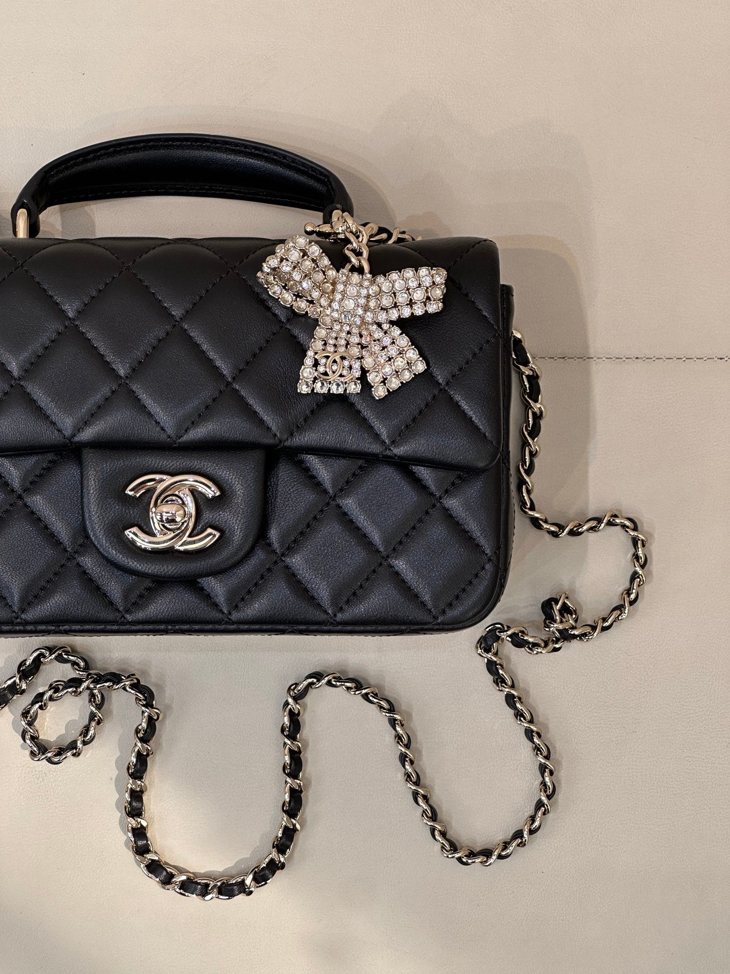 Dark quilted leather flap bag close-up with logo emblem, chain strap, bow clasp