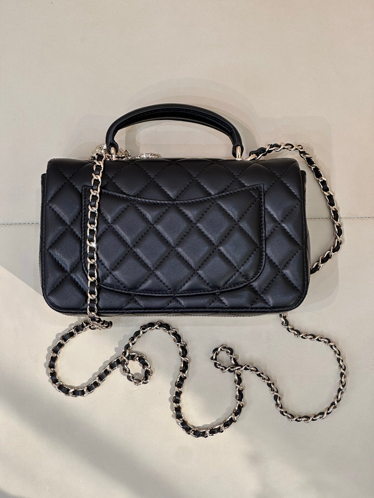Dark quilted leather flap handbag with top handle and chain shoulder straps