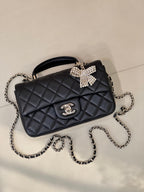 Dark quilted leather mini bag with chain strap and sparkling bow front clasp