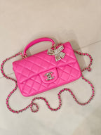 Chanel pink quilted handbag with top handle, chain strap, and rhinestone bow