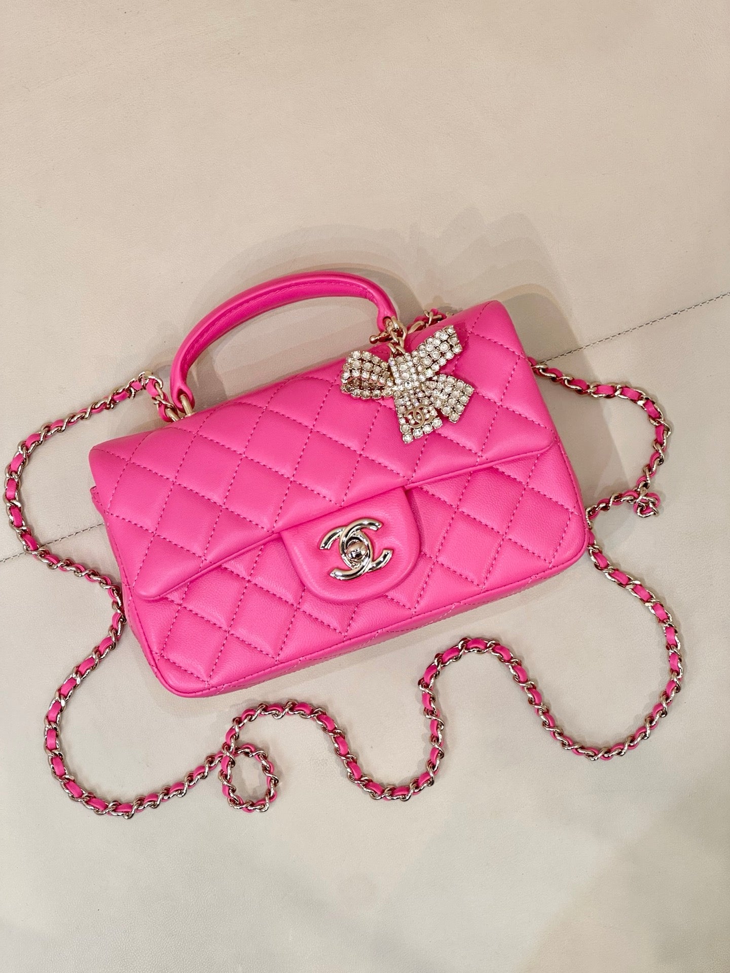 Chanel pink quilted handbag with top handle, chain strap, and rhinestone bow