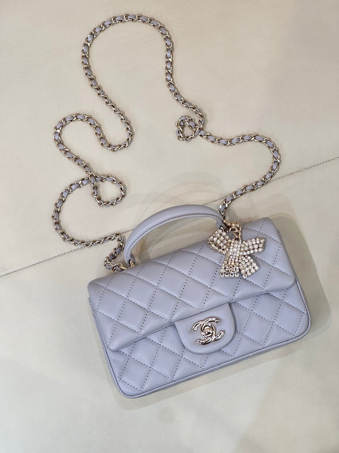 Light blue Chanel quilted crossbody bag with rhinestone bow and gold-tone CC logo.