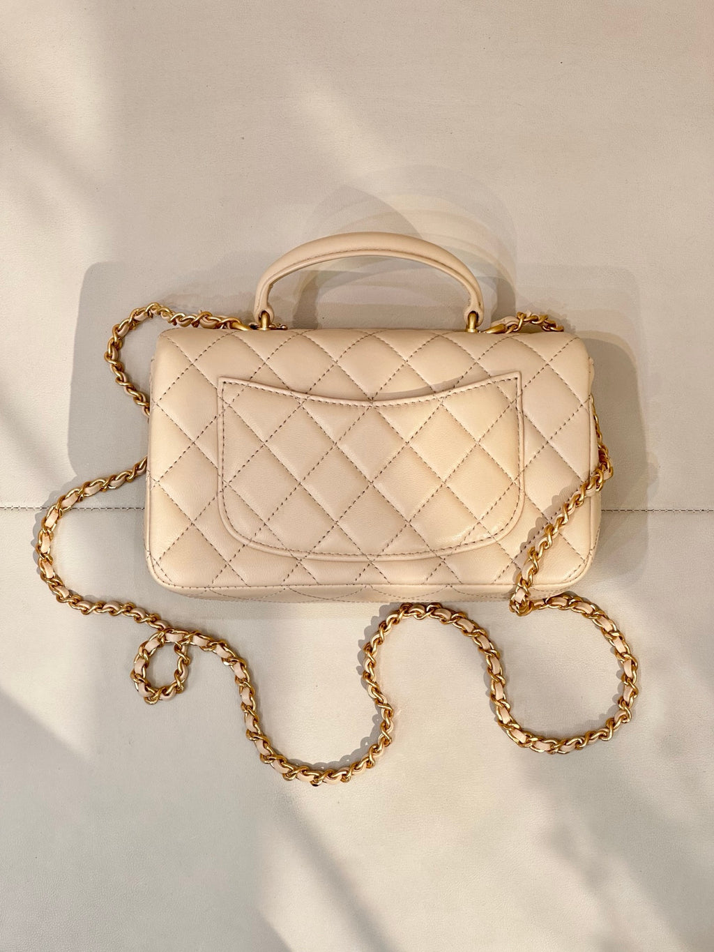Chanel quilted leather bag with top handle, chain strap, and logo flap in light beige