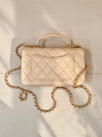 Chanel quilted leather bag with top handle, chain strap, and logo flap in light beige