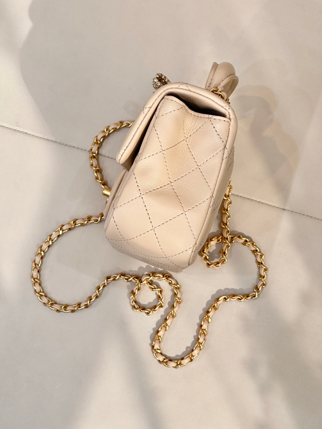Chanel quilted leather bag with chain strap and top handle in light beige, side view