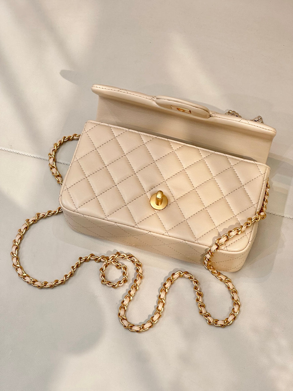 Chanel quilted leather bag with gold-tone turn-lock, chain strap, and top handle in beige