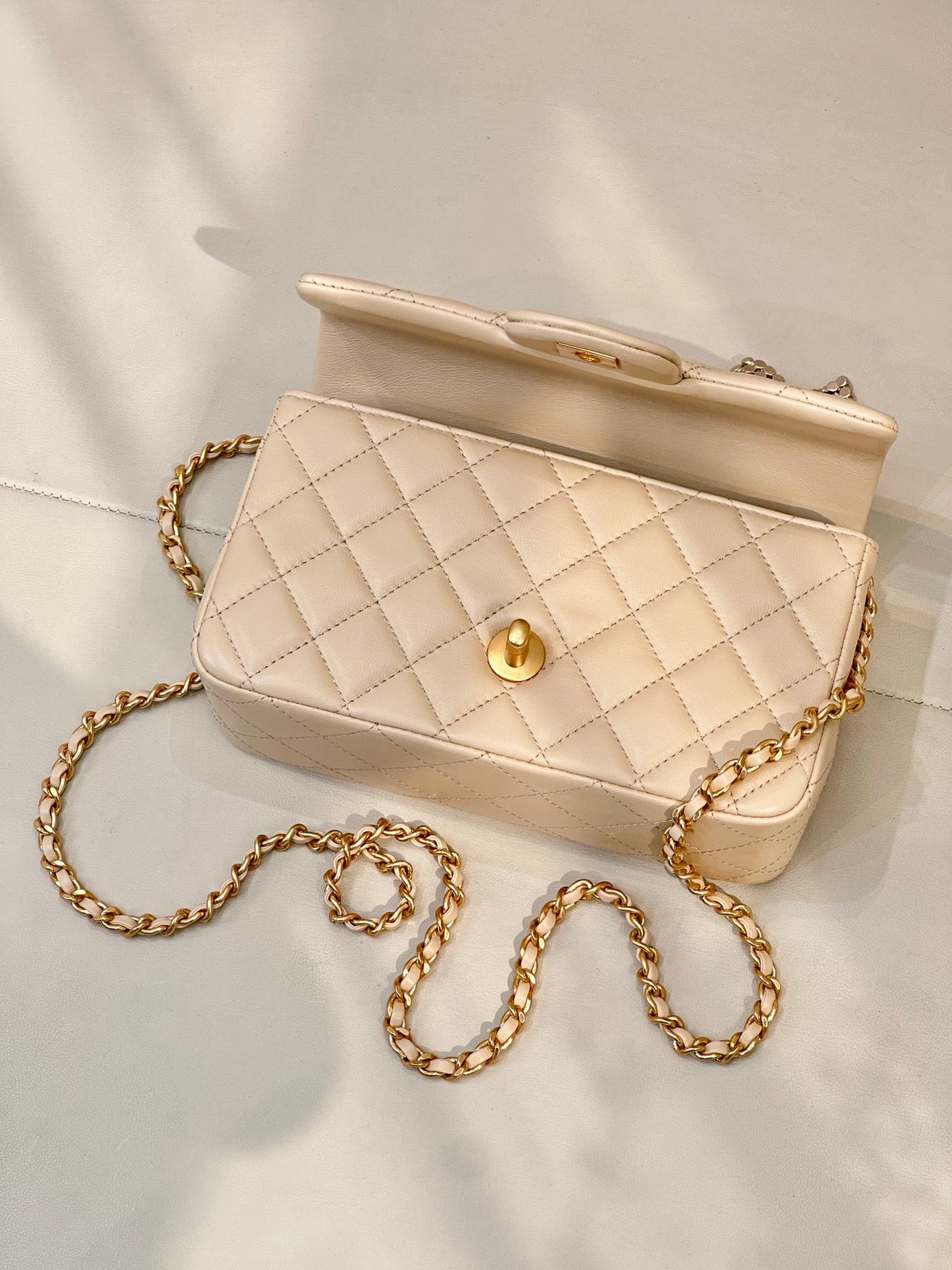 Chanel quilted leather bag with gold-tone turn-lock, chain strap, and top handle in beige